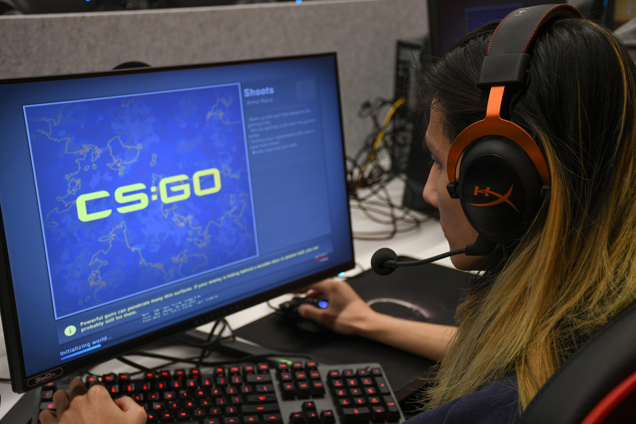 A young man with long hair wears headphones and looks at a loading screen for Counter-Strike: Global Offensive.